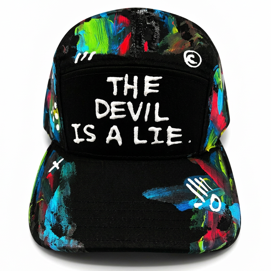 A black baseball cap with a colorful abstract paint splatter pattern on the brim and sides, featuring the text 'THE DEVIL IS A LIE.' in white embroidered letters on the front panel.