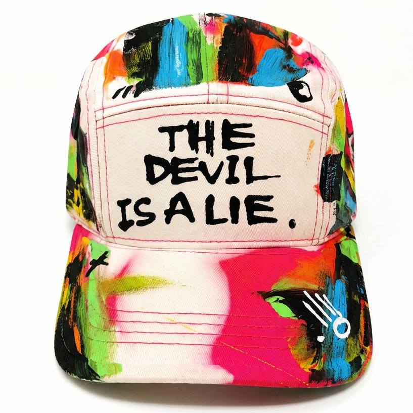 A baseball cap featuring a vibrant, multicolored abstract paint stroke pattern on the brim and sides, with a cream-colored front panel displaying the black embroidered text 'THE DEVIL IS A LIE.'.