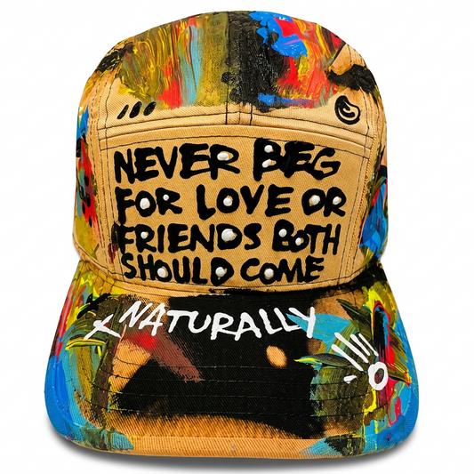 A multicolor abstract art-print baseball cap with a tan denim-texture front panel featuring the text 'NEVER Beg FOR LOVE OR FRIENDS BOTH SHOULD COME' in black, and 'NATURALLY' in white on the brim.