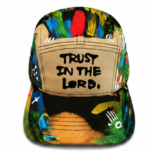 A structured baseball cap featuring a beige front panel with the text 'TRUST IN THE LORD,' surrounded by a vibrant, multicolored abstract paint-splatter pattern in green, blue, yellow, and red.
