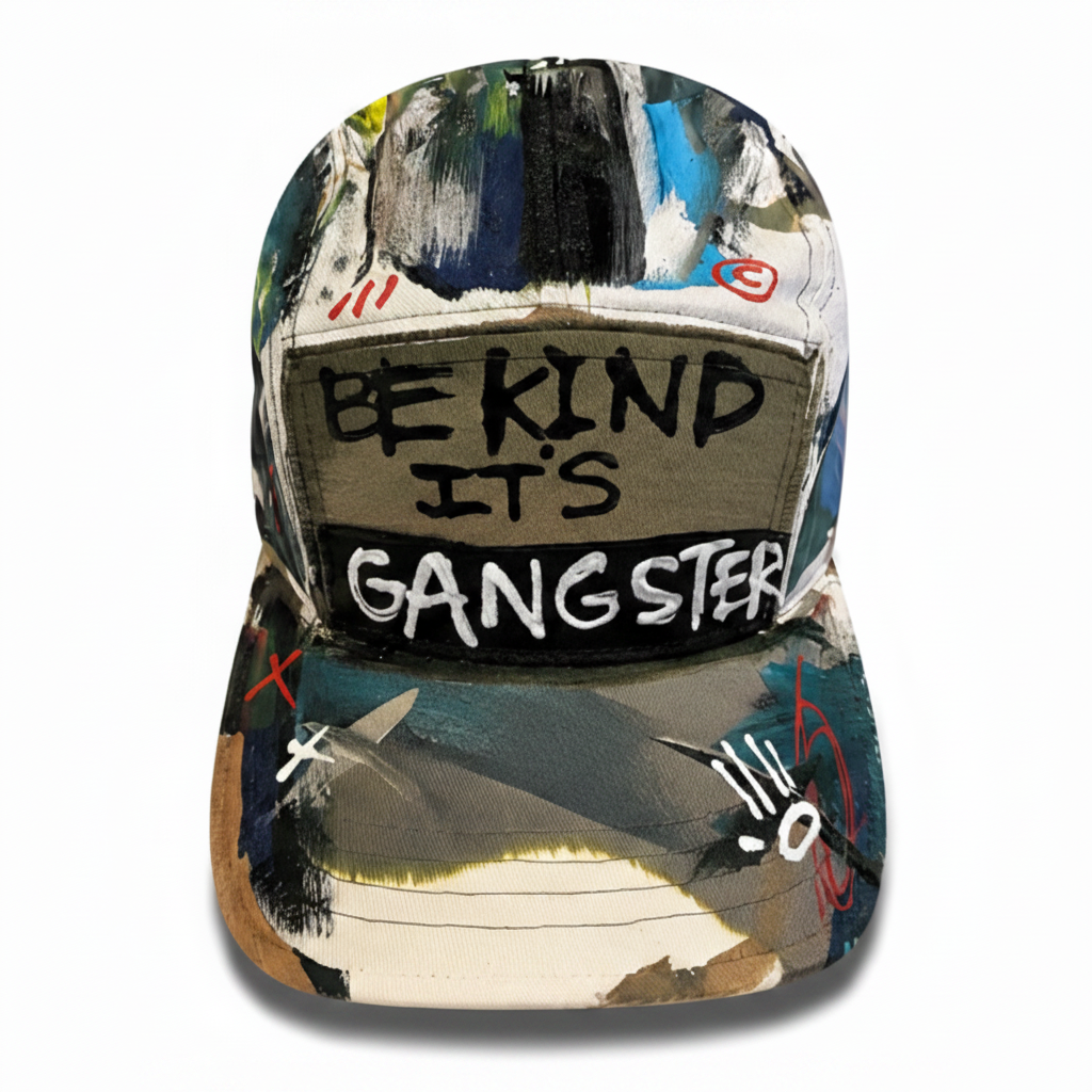 A structured baseball cap featuring a multicolor abstract painted design with a central black patch that reads 'BE KIND IT'S GANGSTER' in white and black lettering.